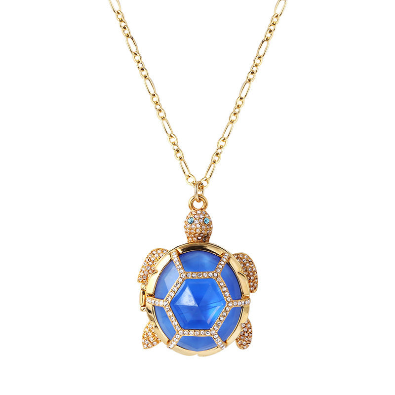 A blue and gold, diamond encrusted turtle pendant hanging on a gold colored necklace