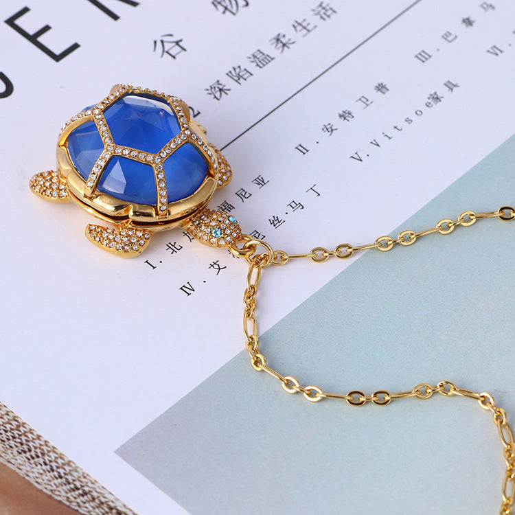 A gold colored blue-shelled turtle necklace lying on some Chinese writing